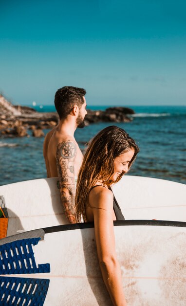 Foto gratuita pareja feliz con tablas de surf de pie cerca del mar