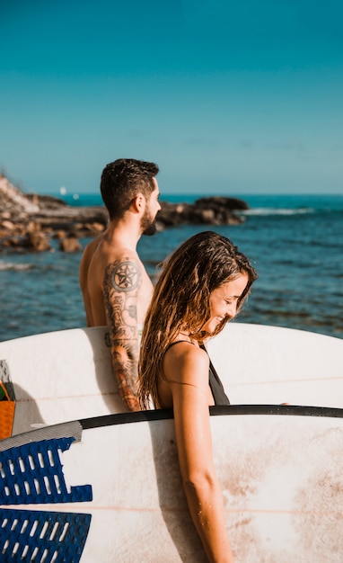 Pareja feliz con tablas de surf de pie cerca del mar