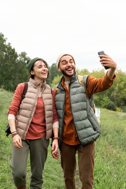 Pareja feliz de tiro completo tomando selfie en la naturaleza con smartphone