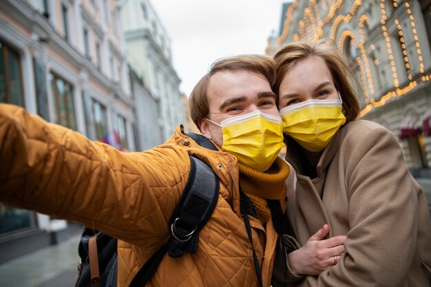 Pareja feliz de tiro medio con máscaras tomando selfie