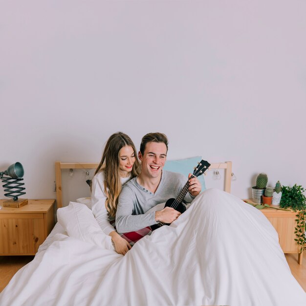 Pareja feliz tocando el ukelele en la cama