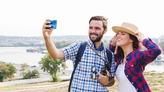 Pareja feliz tomando selfie en teléfono inteligente al aire libre