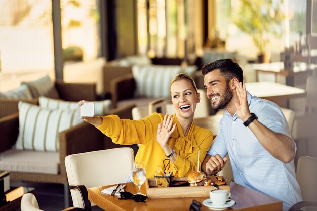 Pareja feliz tomando selfie con teléfono inteligente mientras come en un restaurante