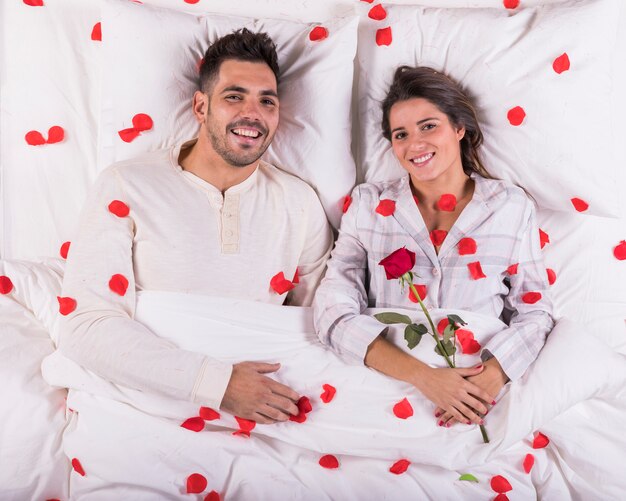 Pareja feliz tumbado en la cama con pétalos de rosa