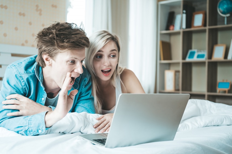Foto gratuito pareja feliz usando la computadora portátil en la cama