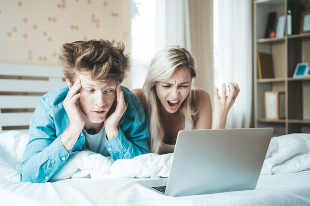 Pareja feliz usando la computadora portátil en la cama