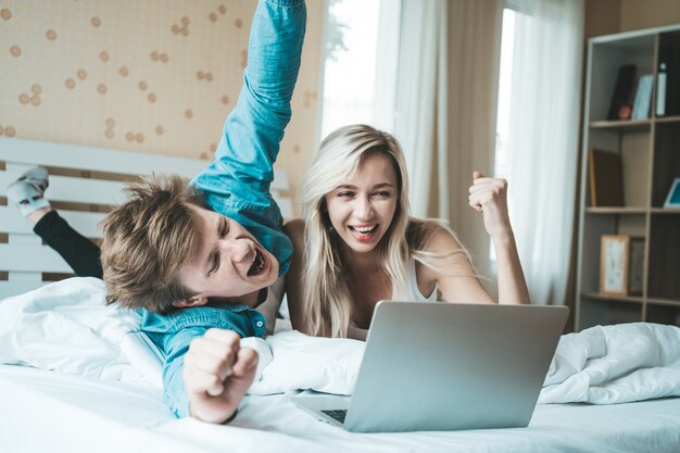 Pareja feliz usando la computadora portátil en la cama