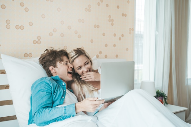 Pareja feliz usando la computadora portátil en la cama