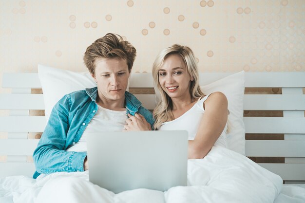 Pareja feliz usando la computadora portátil en la cama