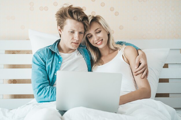 Pareja feliz usando la computadora portátil en la cama