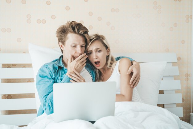 Pareja feliz usando la computadora portátil en la cama