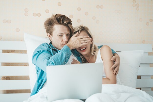 Pareja feliz usando la computadora portátil en la cama