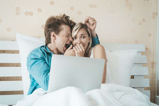 Pareja feliz usando la computadora portátil en la cama