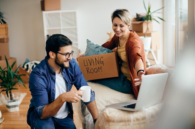 Pareja feliz usando una computadora portátil mientras se muda a un nuevo apartamento