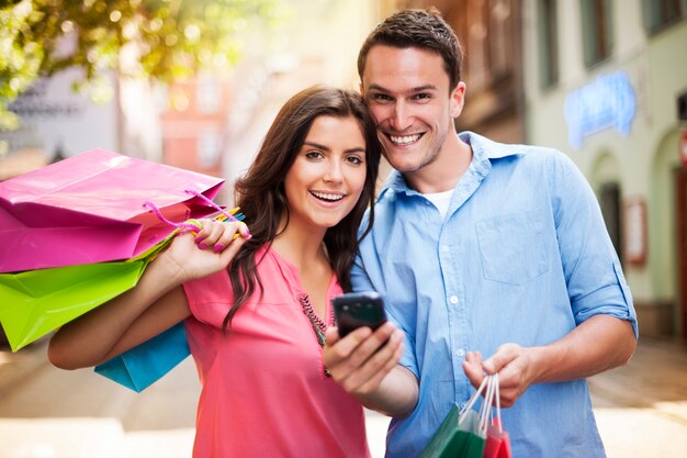 Pareja feliz usando teléfonos inteligentes durante las compras