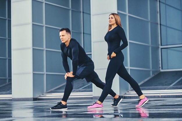 La pareja de fitness atlético se extiende sobre el fondo de un edificio moderno. Imagen de cuerpo completo.