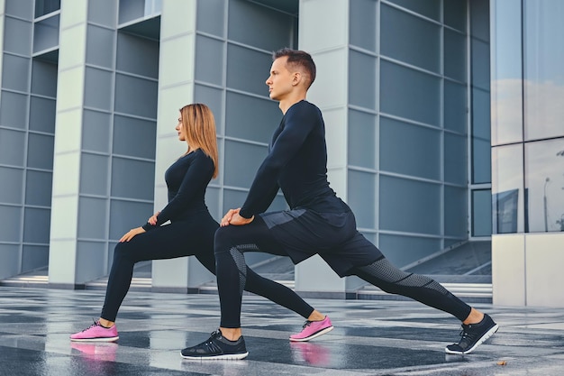 La pareja de fitness atlético se extiende sobre el fondo de un edificio moderno. Imagen de cuerpo completo.