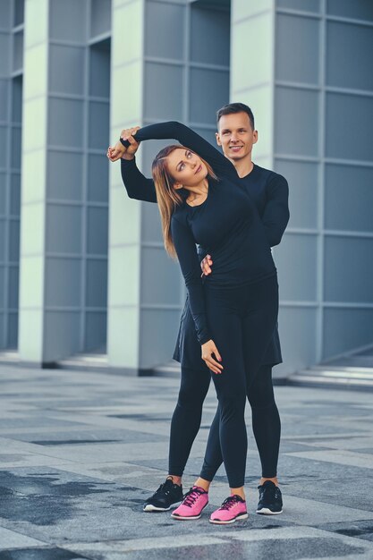 La pareja de fitness atlético se extiende sobre el fondo de un edificio moderno. Imagen de cuerpo completo.