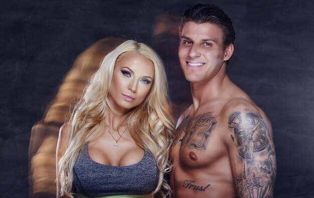 Pareja de fitness. Hombre musculoso tatuado y mujer rubia posando en el estudio.