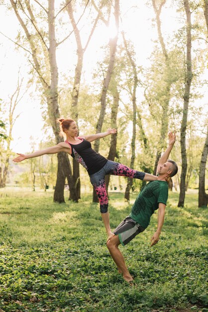 Pareja en forma saludable haciendo acro yoga en pasto