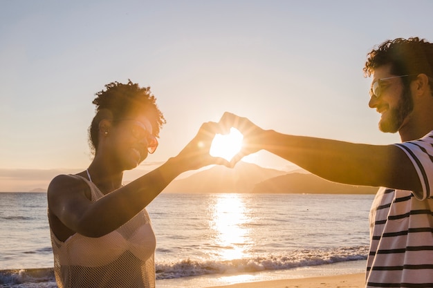 Pareja formando corazón con las manos al atardecer