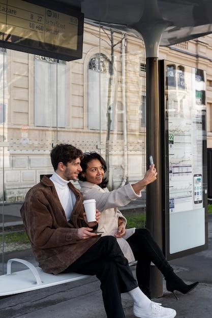 Foto gratuita pareja francesa esperando en la estación para tomar el autobús y tomando un selfie