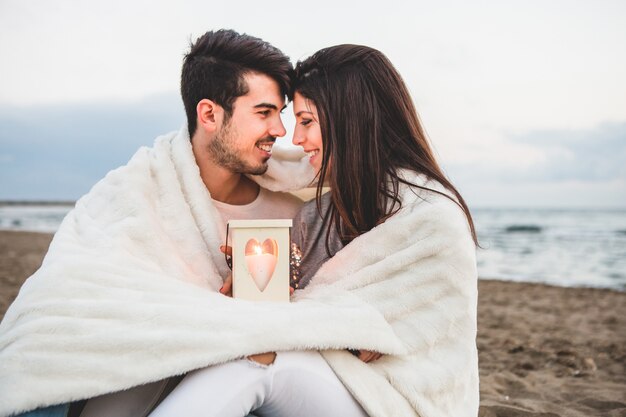 Pareja frente con frente en la arena con una vela y una manta