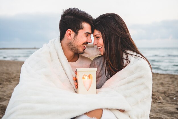 Pareja frente con frente en la arena con una vela y una manta