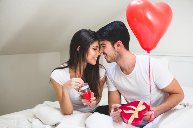 Pareja frente con frente mientras el novio sujeta un regalo y un globo