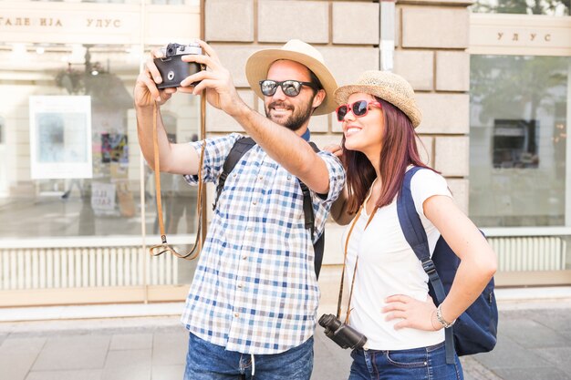 Pareja con gafas de sol y sombrero tomando selfie en cámara