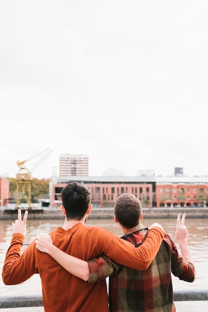 Foto gratuita pareja gay abrazada en el terraplén del río y gesticulando victoria