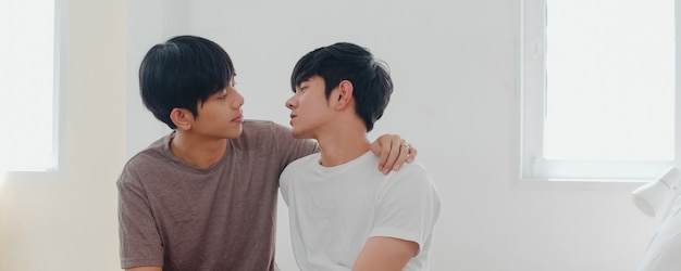 Pareja gay asiática besándose en la cama en su casa. Los jóvenes asiáticos LGBTQ + hombres felices, relajarse, descansar juntos, pasar un momento romántico después de despertarse en la habitación de su casa por la mañana.