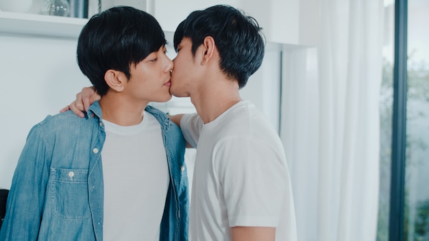 Pareja gay asiática de pie y abrazos habitación en casa. Los jóvenes y guapos hombres LGBTQ + que se besan felices se relajan descansan juntos y pasan un momento romántico en la moderna cocina de la casa por la mañana.