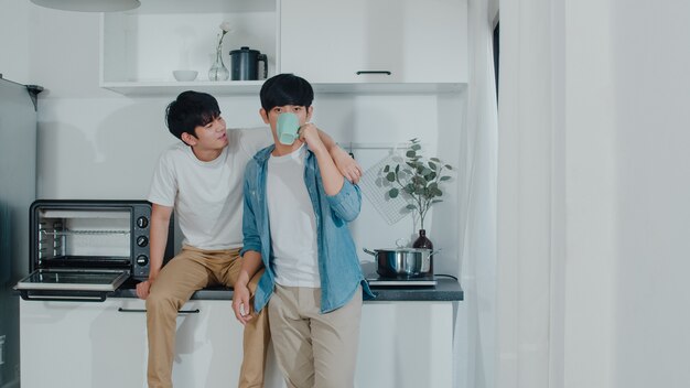 Pareja gay asiática tomando café, pasando un buen rato en casa. Los jóvenes y guapos hombres LGBTQ + que hablan felices se relajan descansan juntos y pasan un momento romántico en la moderna cocina de la casa por la mañana.