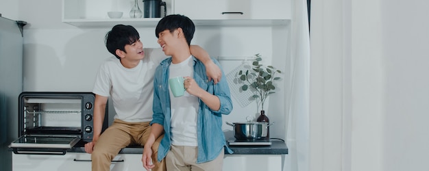 Pareja gay asiática tomando café, pasando un buen rato en casa. Los jóvenes y guapos hombres LGBTQ + que hablan felices se relajan descansan juntos y pasan un momento romántico en la moderna cocina de la casa por la mañana.