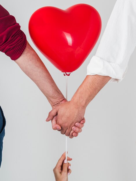 Pareja gay cogidos de la mano con globo para San Valentín