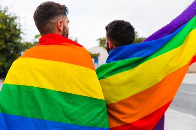 Pareja gay envuelta en banderas LGBT de pie atrás.