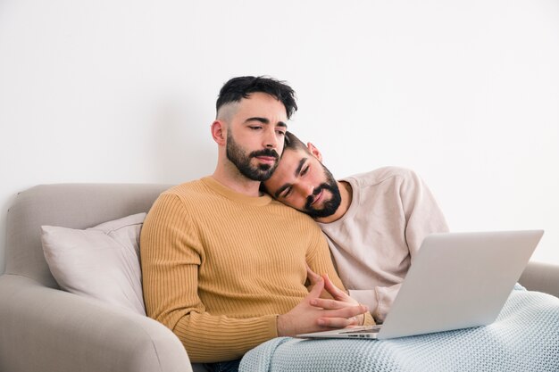 Pareja gay guapo sentados juntos en el sofá mirando portátil