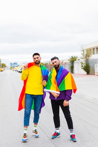 Pareja gay de pie con la bandera del arco iris en la carretera