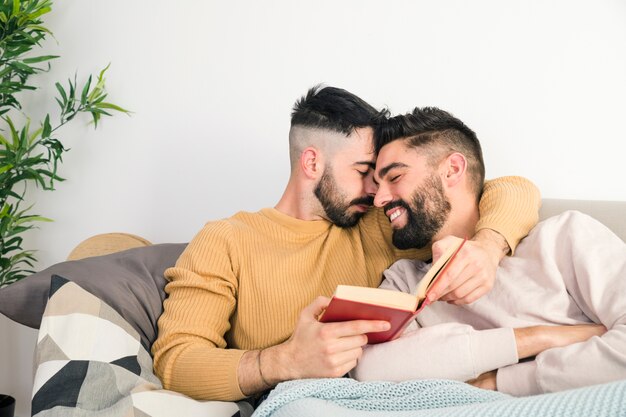 Pareja gay romántica acostado en el sofá contra la pared blanca