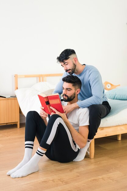 Pareja gay sentada con su novio leyendo el libro en el dormitorio