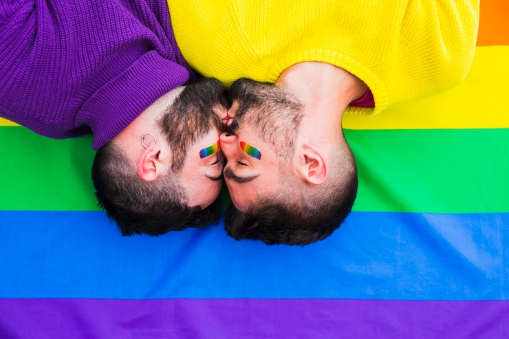 Foto gratuito pareja de gays jóvenes besándose en la bandera del arco iris