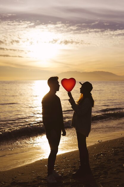 Pareja con globo de corazón en la orilla del mar en la noche