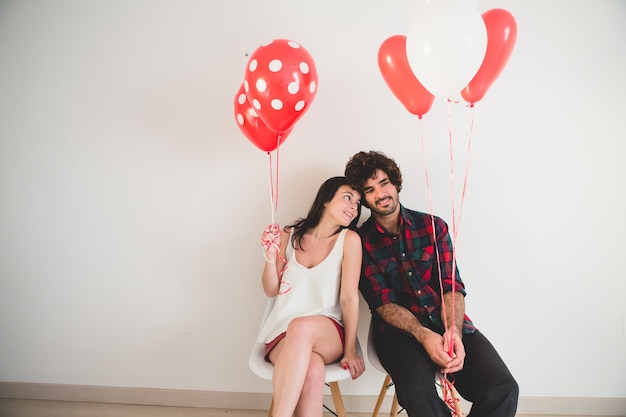 Pareja con globos en las manos sentados en sillas blancas