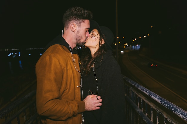 Foto gratuita pareja en guirnalda besándose en calle oscura