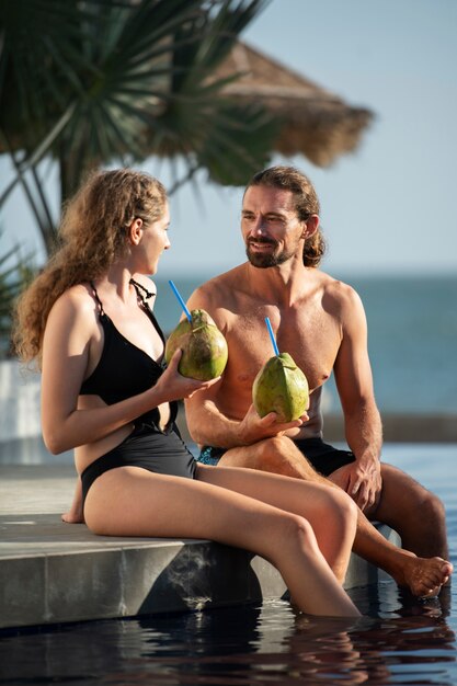 Pareja hablando y bebiendo leche de coco junto a la piscina durante las vacaciones