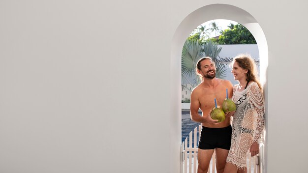 Pareja hablando y bebiendo leche de coco junto a la piscina durante las vacaciones