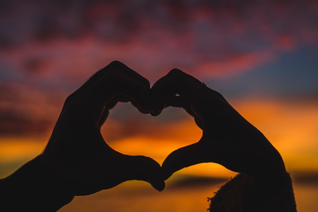 Pareja haciendo forma de corazón de manos en la orilla del mar