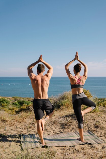 Pareja haciendo yoga en la playa vista trasera