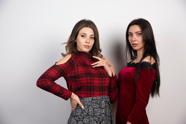 Pareja de hermosas mujeres de pie juntos y posando en la pared blanca.